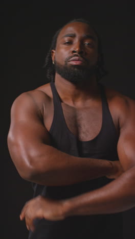 vertical video portrait of serious male athlete wearing fitness vest with muscular physique walking towards camera and into focus training for sports event against black studio background