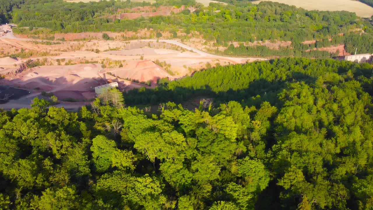 Fast Rotating Shot Over Deep Quarry Excavating Stone Sand Gravel with Thick Forest Treeline. Heavy Mining Excavating Industry Surrounded by Natural Environment