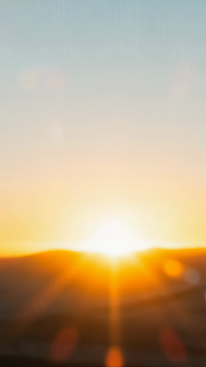 Vertical video: Horizon glowing signaling sun rising above hills at dawn, with lens flare artifacts