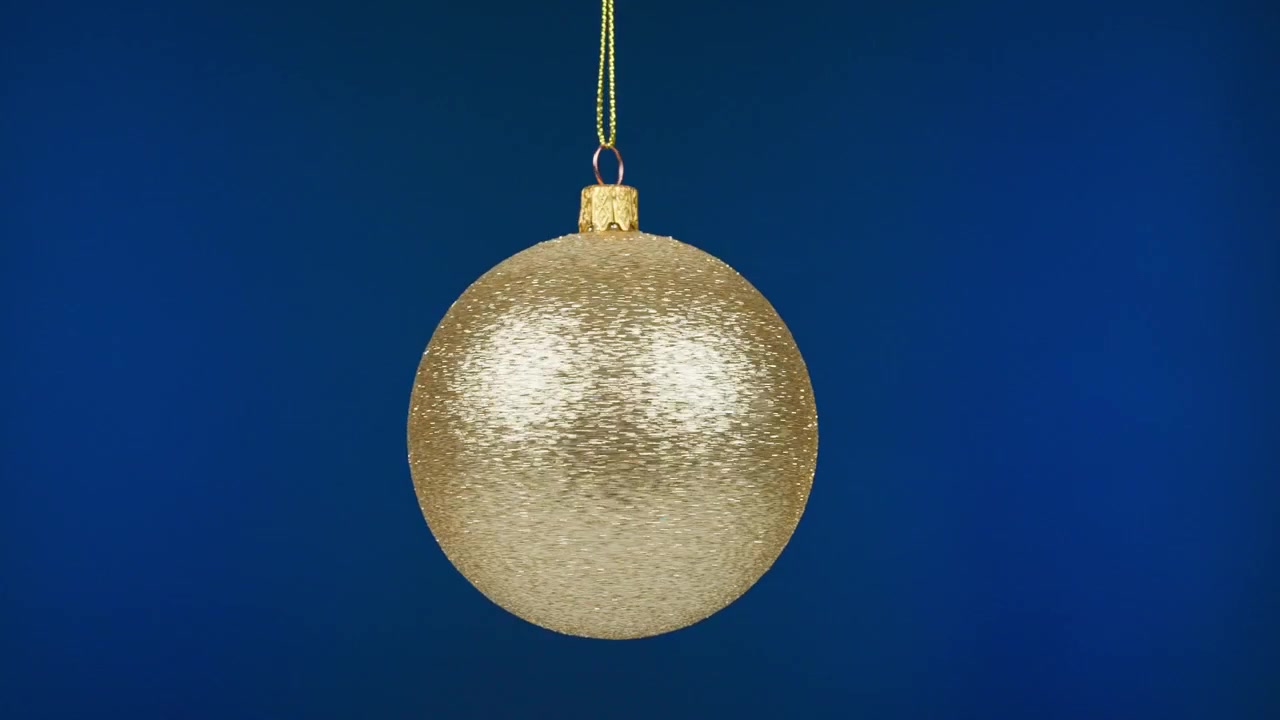 Goldene Glitzer-Weihnachtskugel hängt und schwingt auf blauem Hintergrund