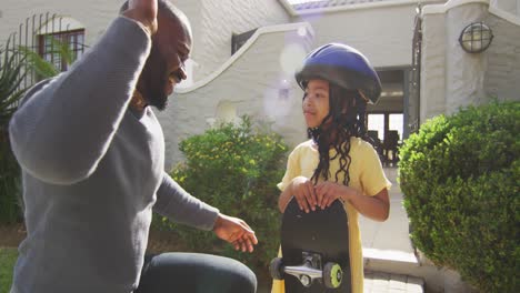 feliz padre afroamericano dando los cinco a su hija sosteniendo un skateboard
