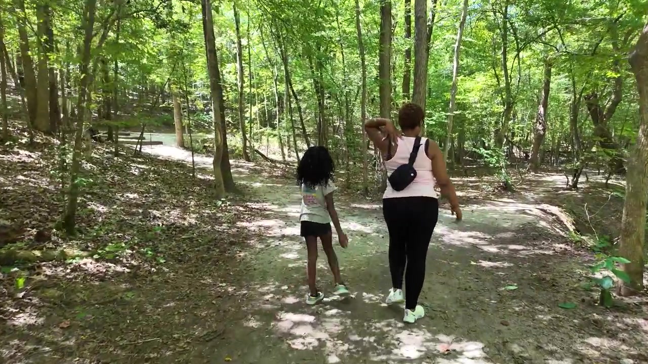 Mulher e criança caminhando em trilha na floresta no verão.