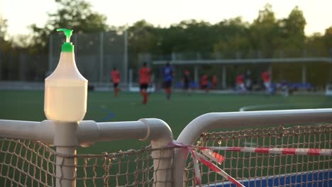 bottle of hand sanitizer on fence beside hockey field, close up truck shot