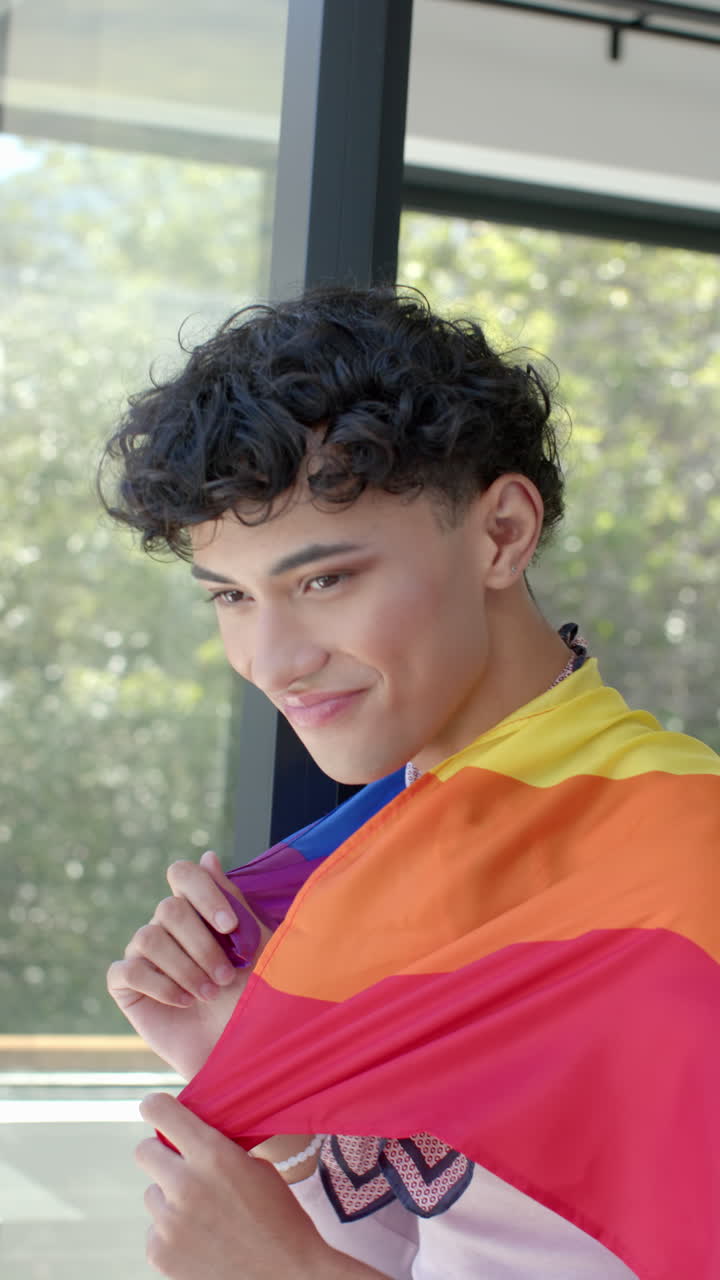Vertical video: Proudly embracing identity, person wrapped in vibrant rainbow flag at home