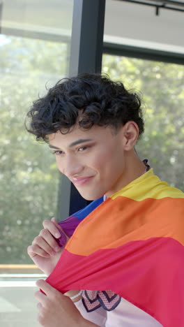 vertical video: proudly embracing identity, person wrapped in vibrant rainbow flag at home