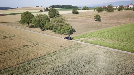 A-volvo-car-drives-in-between-agriculture-fields-in-Swiss-countryside,-mavic-drone-view