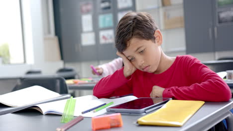 in school, young boy wearing a red shirt leaning on his hand with copy space in the classroom