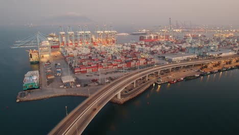 highway curving around stacked shipping containers and loading cranes at port of algeciras, cadiz aerial orbiting view