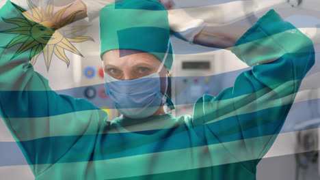 animation of waving uruguay flag against caucasian female surgeon wearing surgical mask at hospital