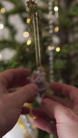 una foto de manos examinando un pequeño ornamento de santa en un árbol de navidad reluciente