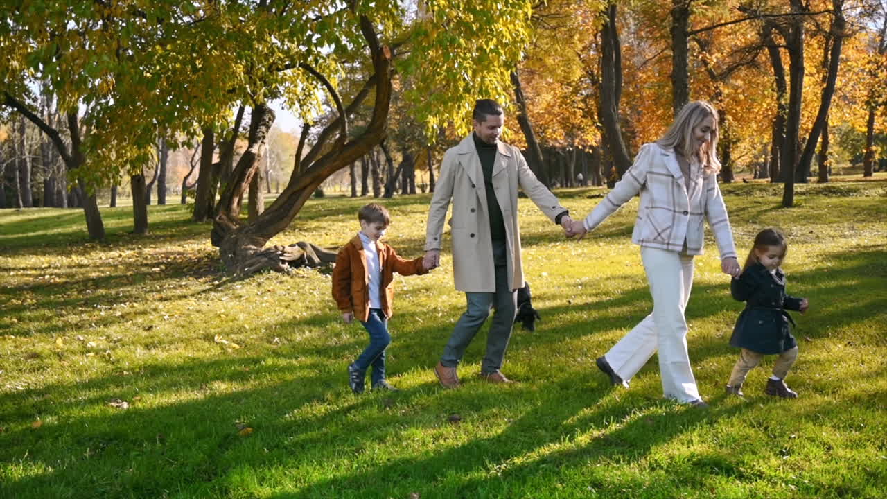 Happy family in an autumn park. Mother and father walking with daughter, son and their dog, yellowed trees around. Slow motion