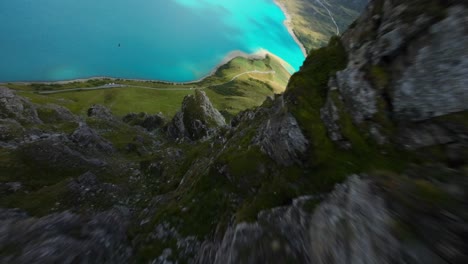 Aerial-FPV-Diving-Down-In-Between-Cliff-Rocky-Side-With-Mont-Cenis-Lake-In-Background