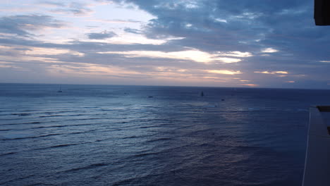 Yates-Navegando-Sobre-Las-Brillantes-Olas-Del-Océano-Durante-La-Puesta-De-Sol,-Vista-Desde-El-Balcón,-Slomo,-Bahía-De-Waikiki