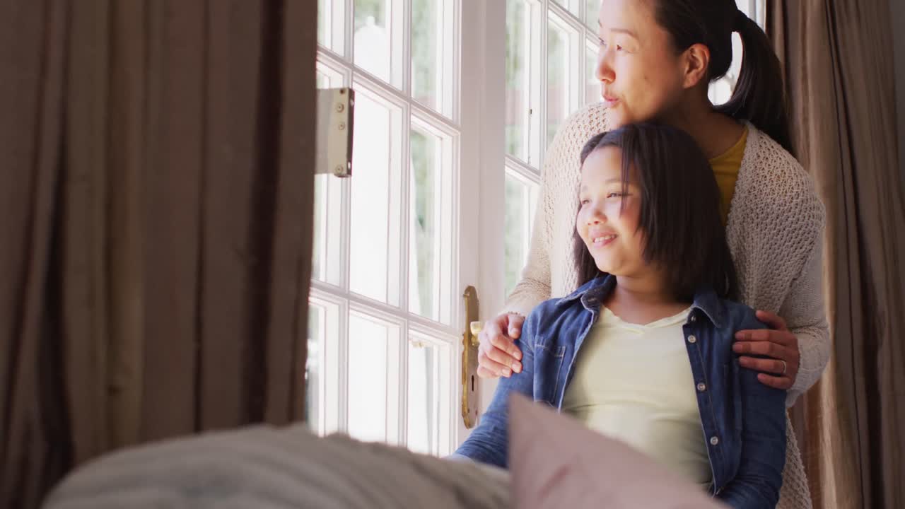 视频：沉思的亚洲妈妈和女儿看向窗外。