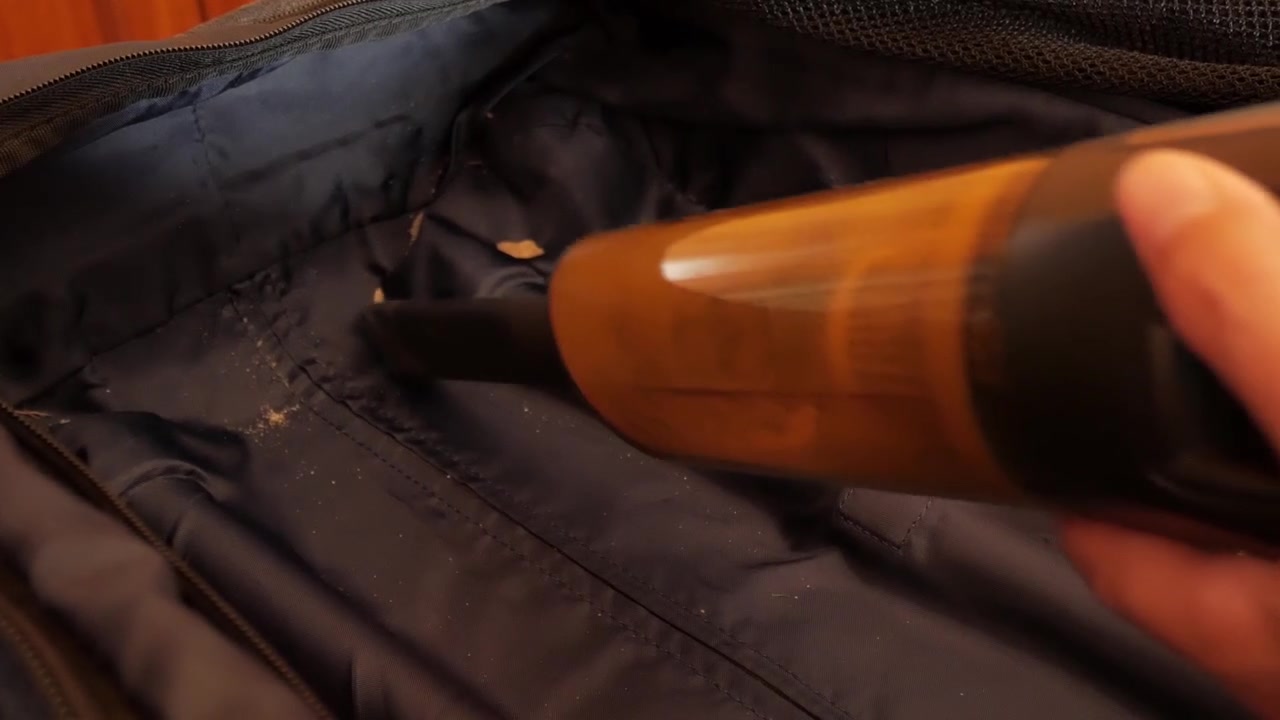 Handheld vacuum cleaning the inside of an empty suitcase, removing visible debris