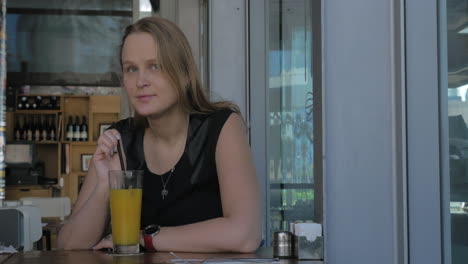una mujer joven y melancólica tomando una copa en un café.