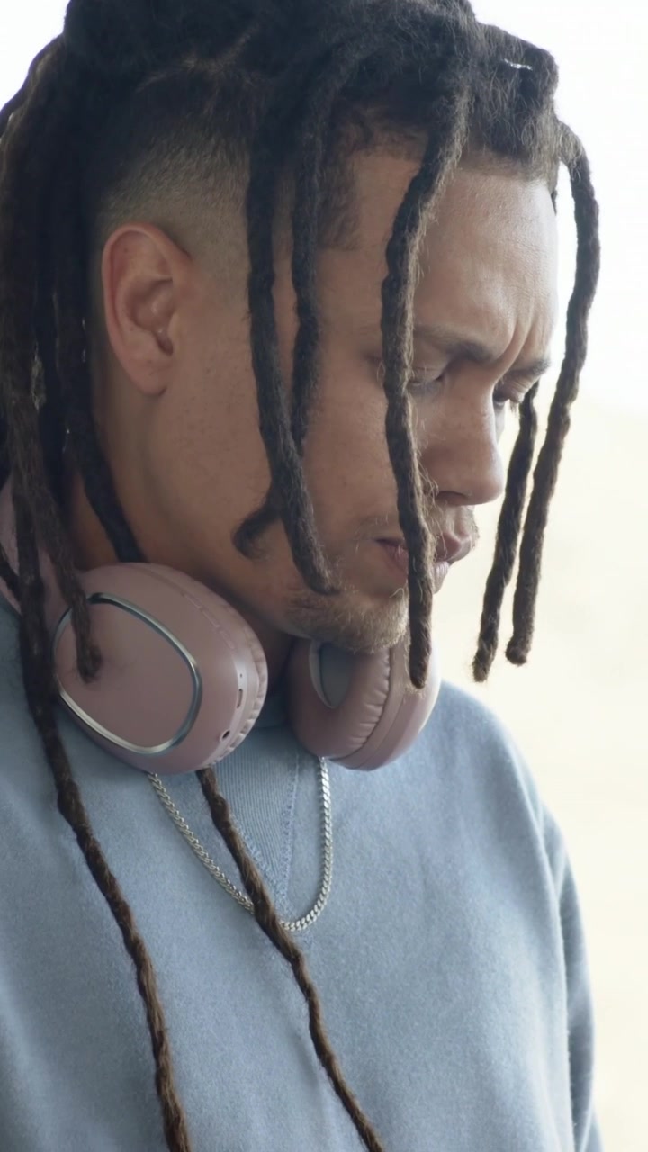 Video verticale: Primo piano di un uomo con i dreadlock che usa il tablet vicino alla finestra, leggendo, con una maglietta blu e cuffie.