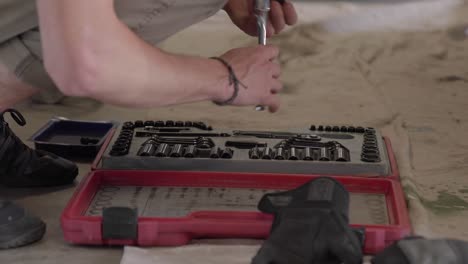 young man tests ratchet sockets from tool set on floor of tidy garage