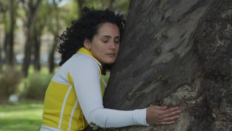 cerca de una joven y atractiva activista morena abrazando un árbol con los ojos cerrados en un parque