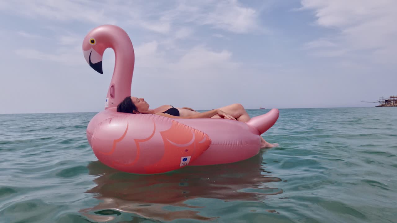 mujer con traje de baño bikini relajándose en un flamenco rosa inflable flotando en la superficie del agua del mar
