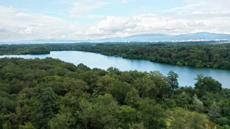 Blauer-See-Zwischen-Den-Dichten-Wäldern-Einer-Westeuropäischen-Landschaft-Unter-Bewölktem-Himmel,-Drohnen-Luftaufnahme