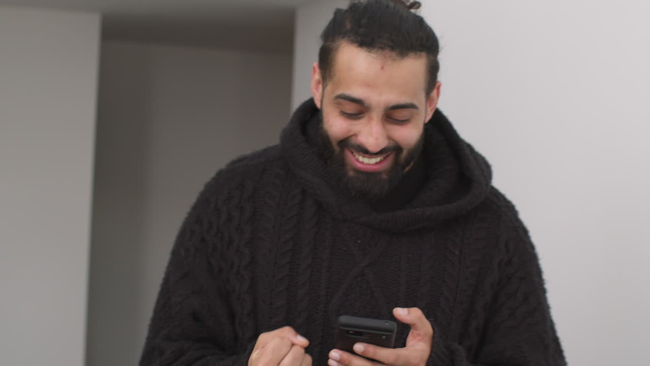 Scatto di giovane uomo con telefono cellulare che celebra la vincita di denaro su sfondo grigio