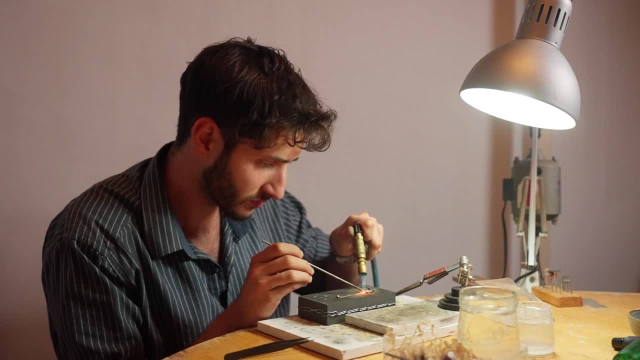 un artesano en el proceso de diseñar una pequeña pieza de arte centrada en los detalles intrincados en un espacio de trabajo bien equipado iluminado por una lámpara.