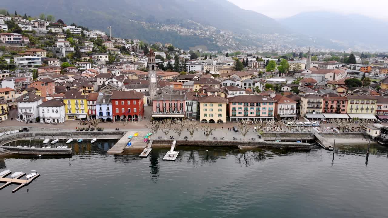 sobrevuelo aéreo con un giro desde las orillas del lago maggiore sobre el paseo marítimo de ascona en ticino, suiza sobre los tejados alrededor de la torre de la iglesia que revela el lago y las montañas