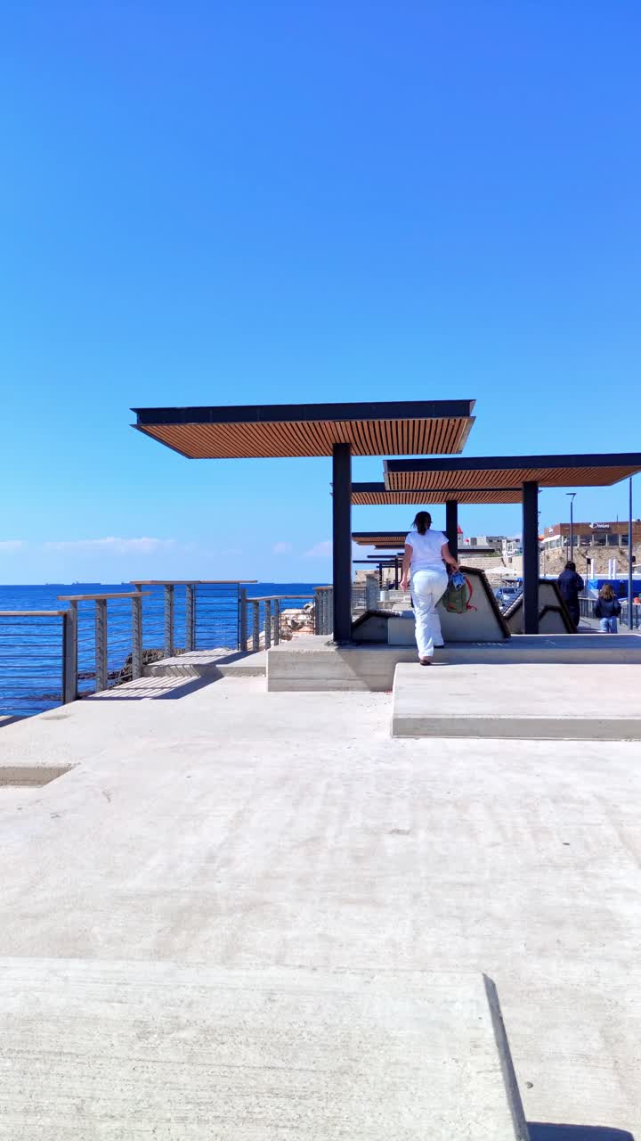 Donna che cammina verso una moderna struttura a pergola sul lungomare