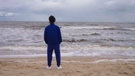 back view of a punjabi sikh man in front of a beach with rough waves