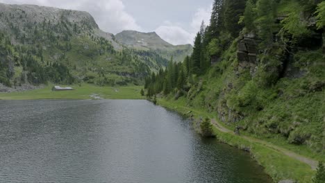 Drone-shot-of-cyclist-riding-along-lake-shore-and-greened-Dolomites-during-summer