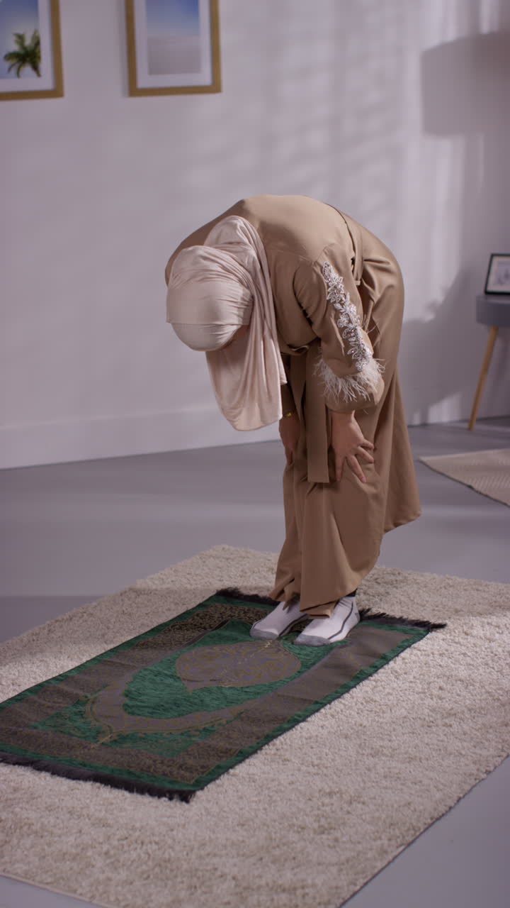 Vertikal video av muslimsk kvinne med hijab som ber knelende på bønneteppe hjemme 4