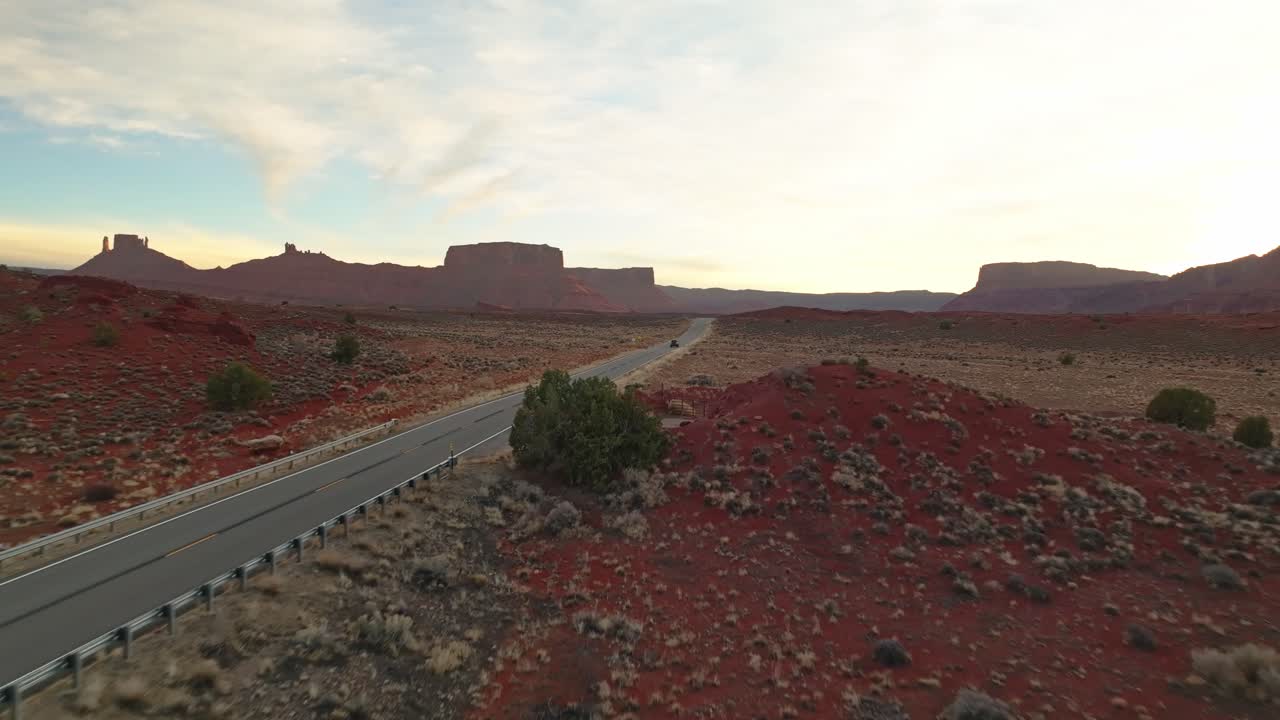 Dramatic contrast between sunlit cliffs and shaded valley floor in sweeping canyon landscape, aerial dolly along desert road in Moab Utah USA