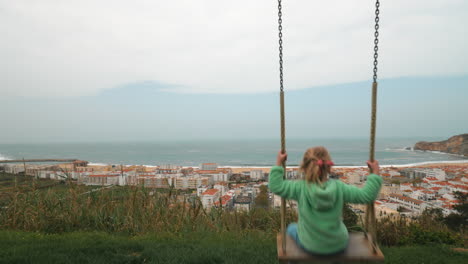 Niña-Mirando-El-Océano-Y-La-Ciudad-Turística-Desde-El-Columpio-Nazaré-En-Portugal