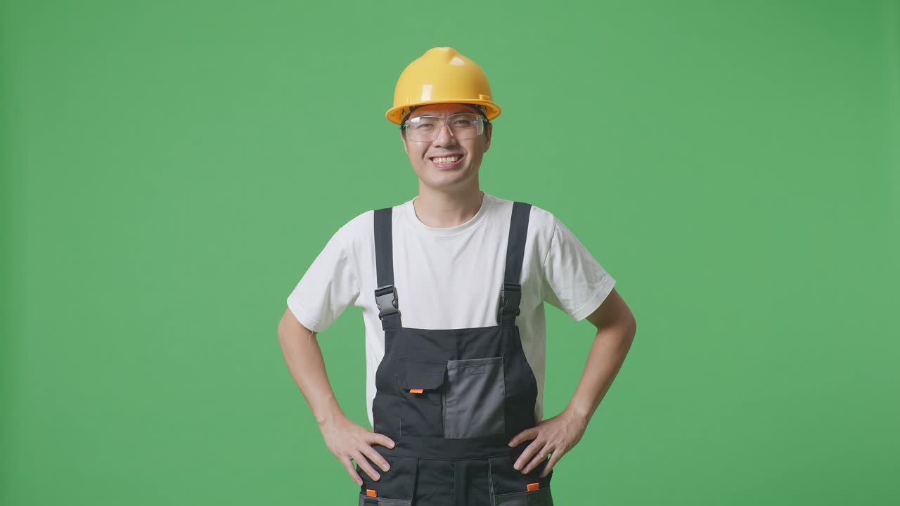 Asian Man Worker Wearing Goggles And Safety Helmet Standing With Arms Akimbo Looking At Camera And Smiling In The Green Screen Background Studio