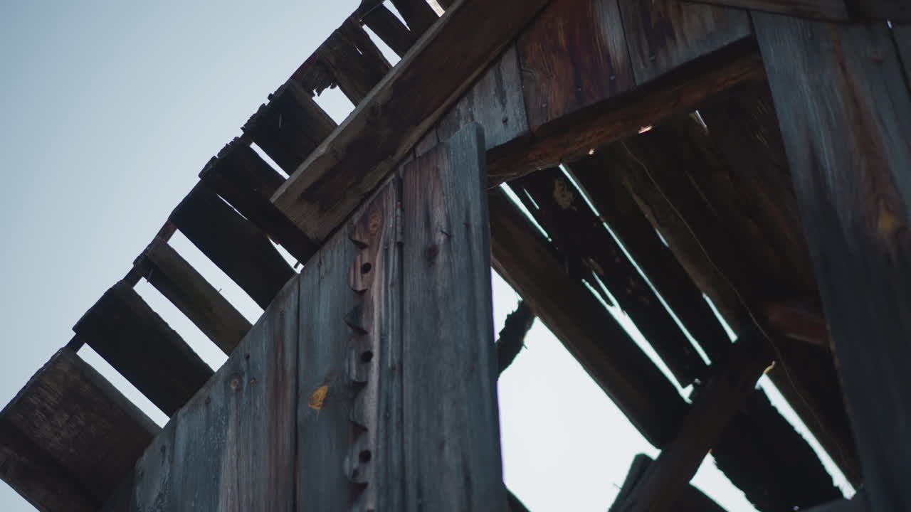 Weathered barn rafters with deep shadow, closeup of aged wood planks and exposed nails, gritty grain and cool toning, architectural study of decay suggesting documentary or restoration planning
