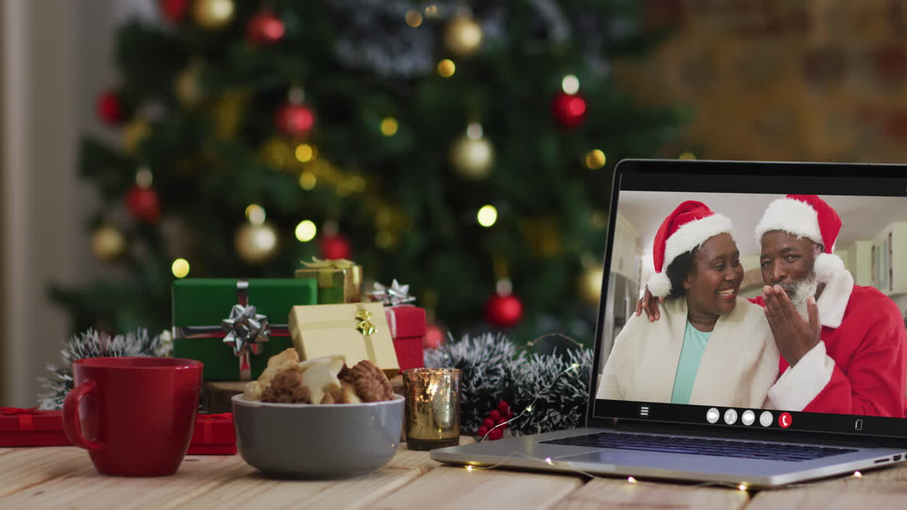 una pareja de ancianos afroamericanos con sombreros de santa en una videollamada en una computadora portátil, con un árbol de navidad