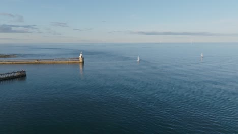 two yachts sailing calm blue sea close to white lighthouse
