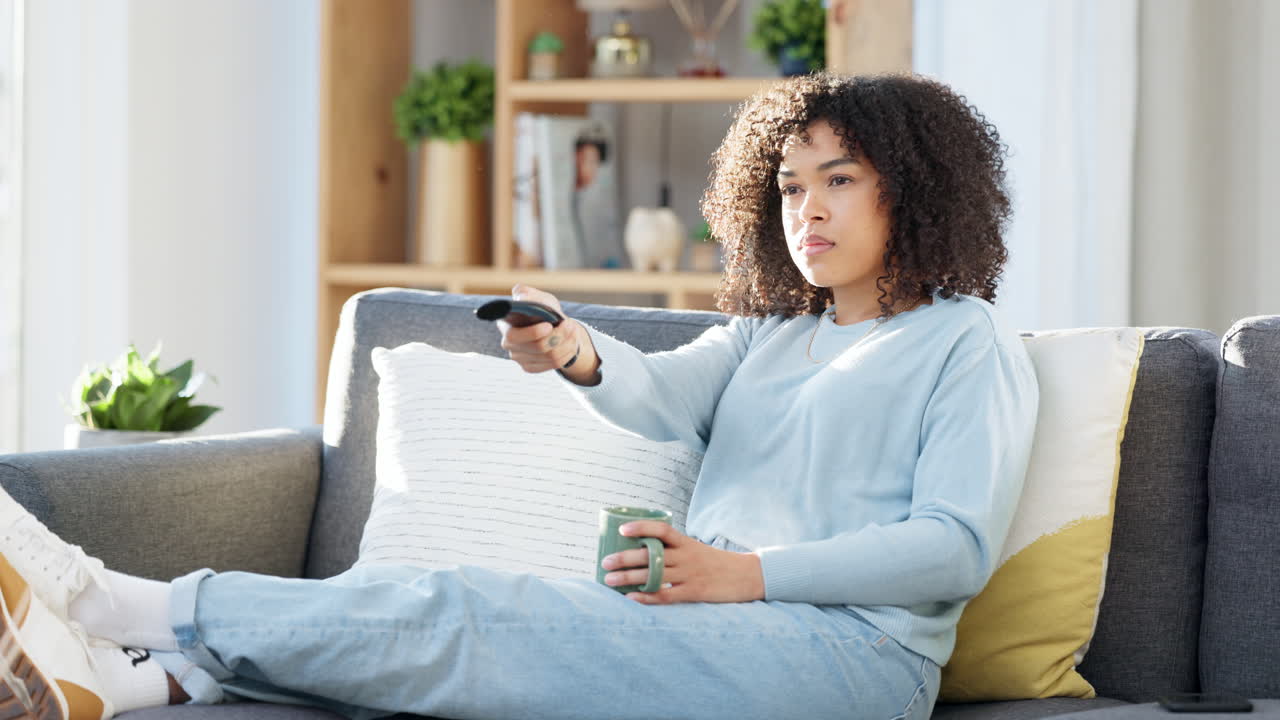 흑인 여성이 tv를 보고 커피를 마시고 있습니다.