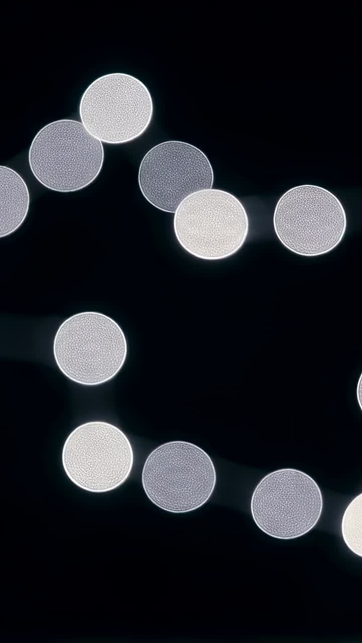 Video verticale: cambio di angolazione della camera che rivela parti di luci bokeh LED su una stringa contro un filo nero