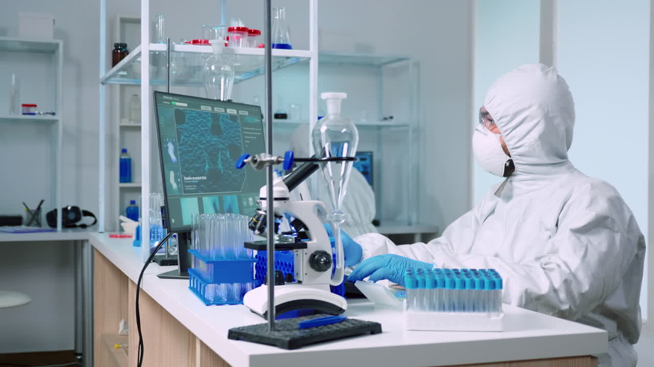 Chemist in protection suit examining various bacteria holding petri dish
