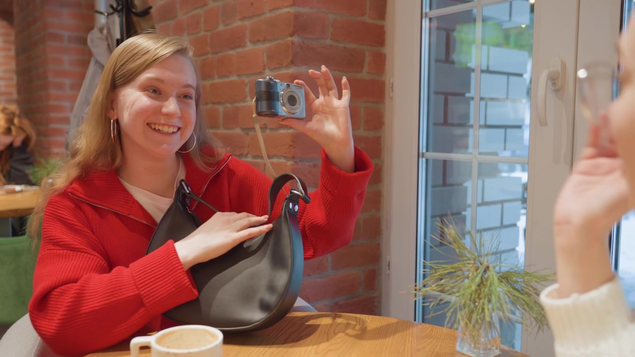 Giovane donna estrae una fotocamera digitale dalla borsa in un caffè.
