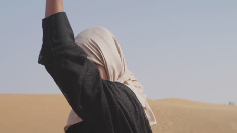 donna musulmana in hijab che muove dolcemente la mano in un deserto ventoso