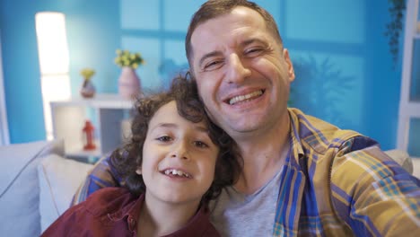 Father-son-sitting-on-sofa-and-talking-on-smartphone-via-video-link.