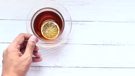 hand holding a cup of lemon tea on a white wooden table