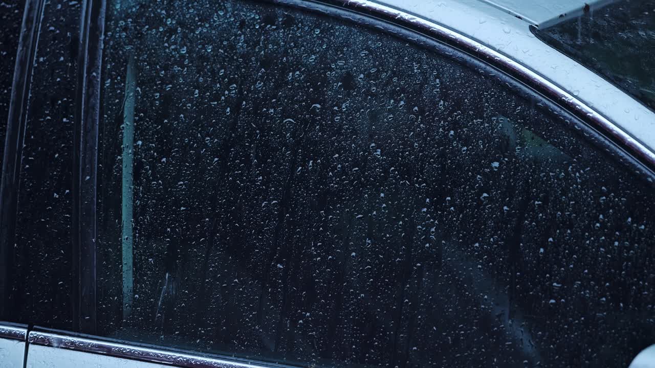 Raindrops trickle across vehicle glass surface in detailed cinematic frame