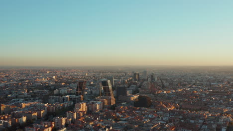 Imágenes-Descendentes-Hacia-Atrás-De-Una-Gran-Ciudad-En-El-Atardecer.-Vista-Panorámica-Aérea-Del-Desarrollo-De-La-Ciudad-Iluminada-Por-Luz-Brillante.