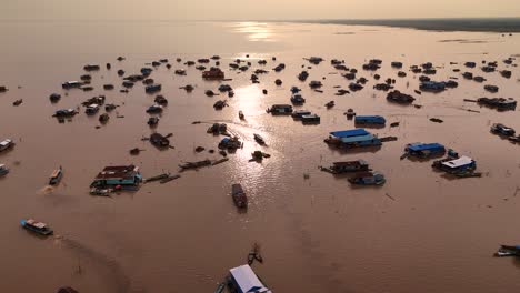 aerial wide over a silhoutted floating village of tonle sap lake, cambodia, unveiling floating houses and boats scattered around.