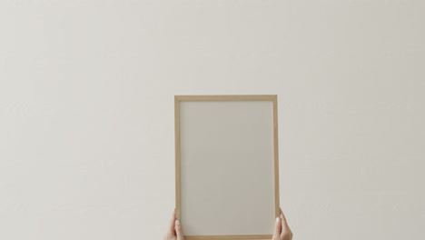 Hands-of-caucasian-woman-holding-frame-with-copy-space-on-white-background-against-white-wall