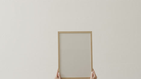 hands of caucasian woman holding frame with copy space on white background against white wall